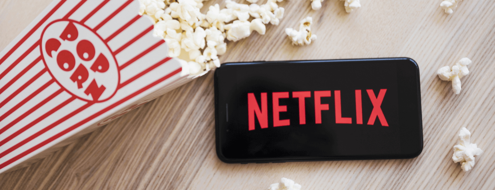 Cellphone with Netflix logo on table next to box of popcorn