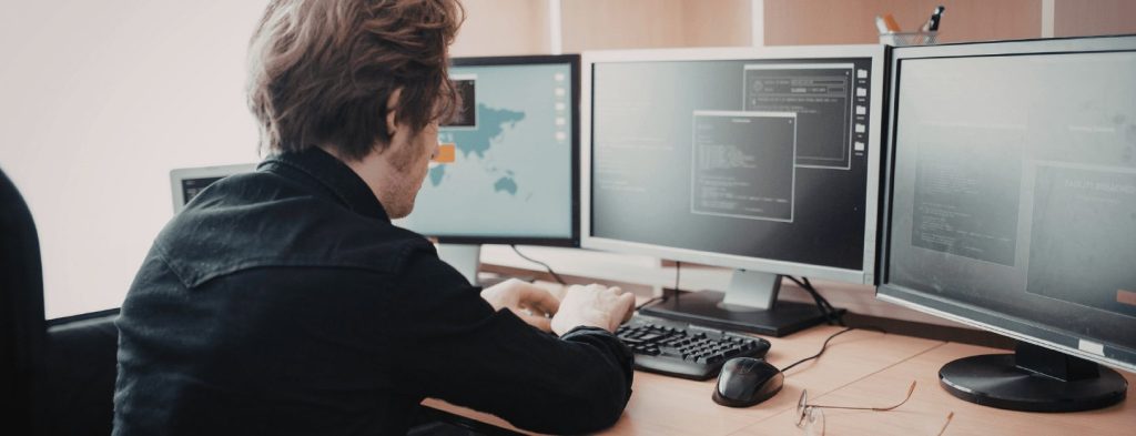 Man is working on his computer, with three screens