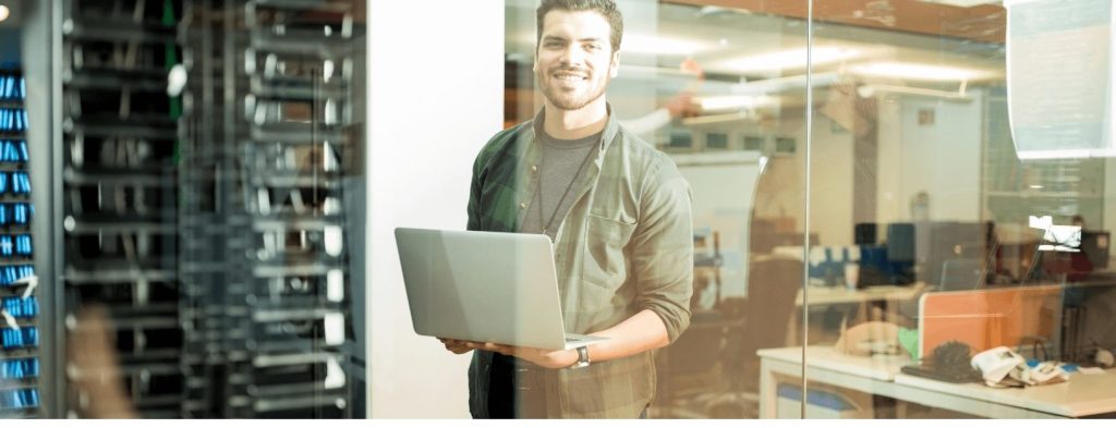 A network engineer smiles at the camera while holding his open laptop