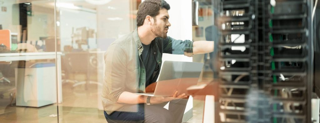 A network engineering is adjusting a server while holding a laptop